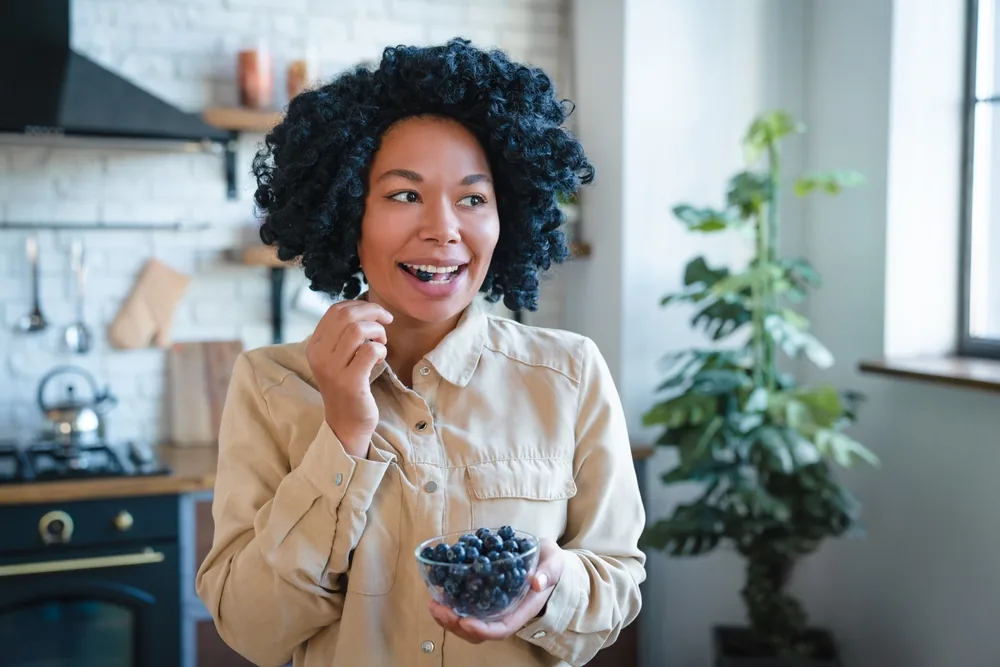 A woman eating blueberries in a kitchen