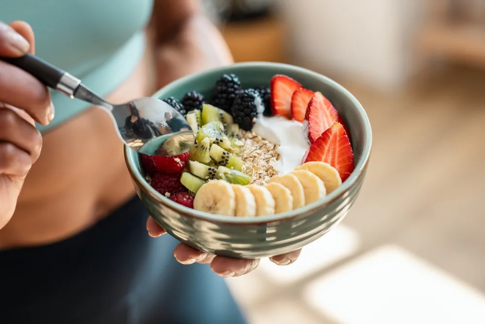 A bowl of fruit, yoghurt and oats held in both hands