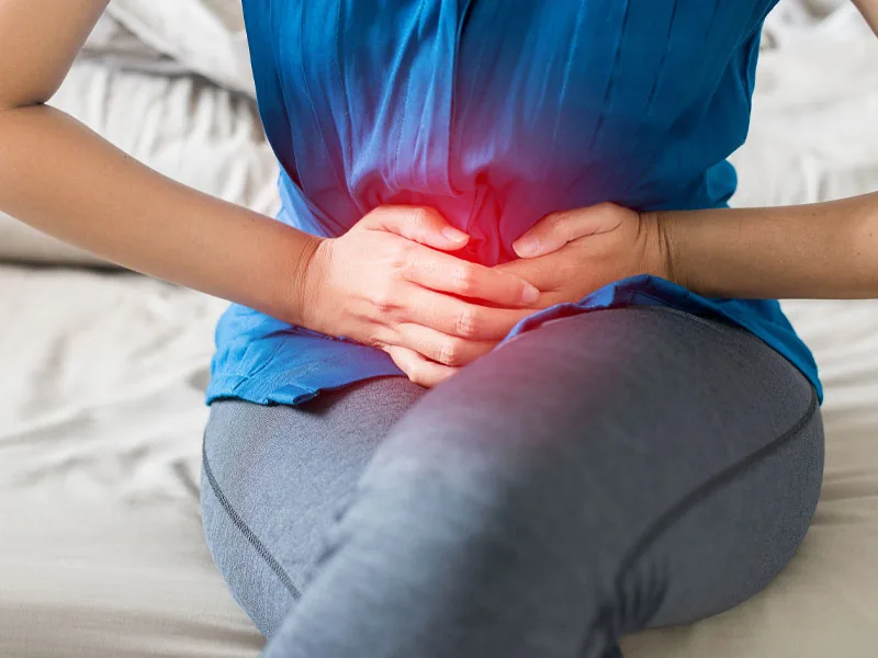 A person seated, hands over the lower abdomen
