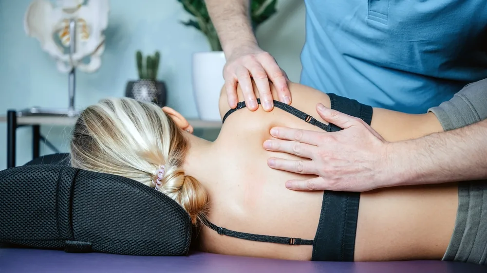A therapist working on a client's upper back in a treatment room